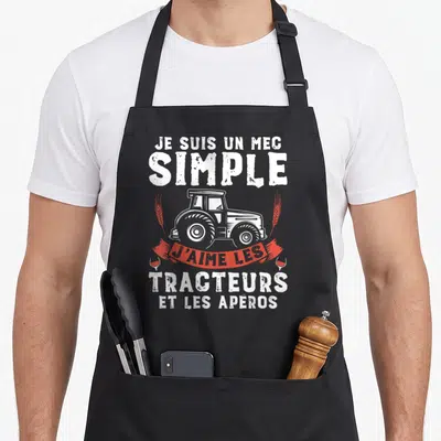 Tablier de cuisine noir avec illustration de tracteur blanc et texte humoristique sur fond gris uni.