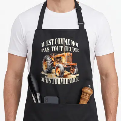 Tablier de cuisine noir avec illustration de vieux tracteur orange et texte Il est comme moi pas tout jeune mais formidable.