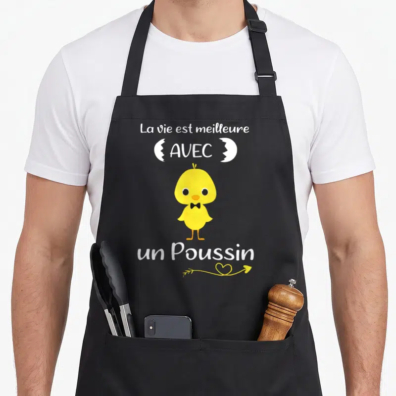 Tablier de cuisine noir avec un poussin jaune portant un nœud papillon et le texte La vie est meilleure avec un Poussin