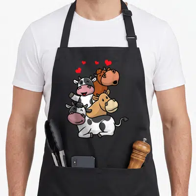 Tablier de cuisine noir avec illustration de quatre vaches de dessin animé et des cœurs rouges flottant au-dessus.