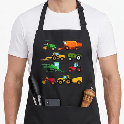 Tablier de cuisine noir avec illustration de tracteurs et machines agricoles aux couleurs vives disposés en grille.