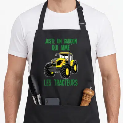 Tablier de cuisine noir avec illustration d'un tracteur jaune et texte vert justant une passion agricole.