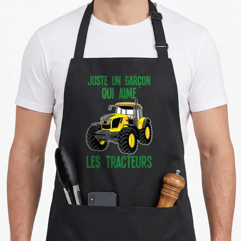 Tablier de cuisine noir avec illustration d'un tracteur jaune et texte vert justant une passion agricole.