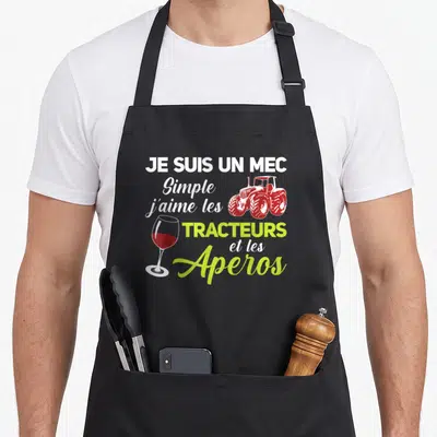 Tablier de cuisine noir avec texte blanc vert et illustrations d'un verre de vin rouge et d'un tracteur rouge stylisé.
