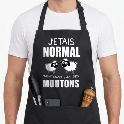 Tablier de cuisine noir avec l'inscription J'étais normal maintenant j'ai des moutons et deux béliers dessinés en noir et blanc.