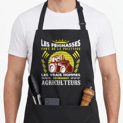 Tablier de cuisine noir avec illustration de tracteur et texte humoristique sur l'agriculture et la politique.