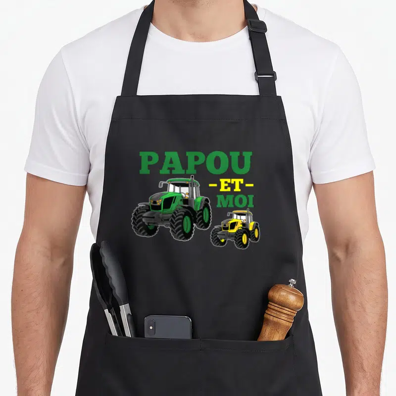 Tablier de cuisine noir avec l'inscription Papou et moi surplombant deux tracteurs verts et jaunes stylisés.