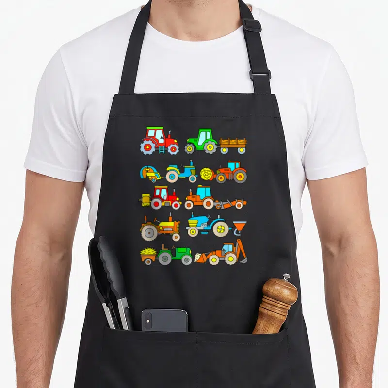 Tablier de cuisine noir avec une illustration de cinq rangées de tracteurs aux couleurs vives et des machines agricoles stylisées.