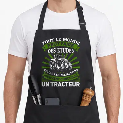 Tablier de cuisine noir avec inscription humoristique sur la conduite du tracteur et dessin blanc du véhicule agricole au centre.