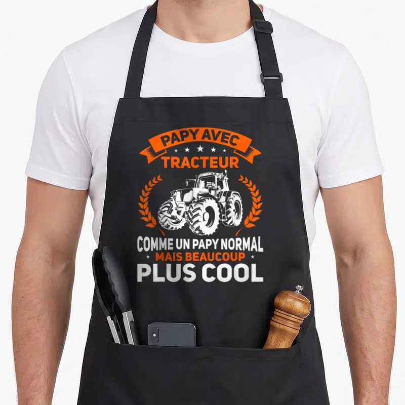Tablier de cuisine noir avec illustration de tracteur blanc et texte orange proclamant être un papy avec tracteur plus cool que la normale.