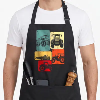 Tablier de cuisine noir avec cinq rectangles colorés affichant des silhouettes de tracteurs dans un style graphique vintage et délavé.