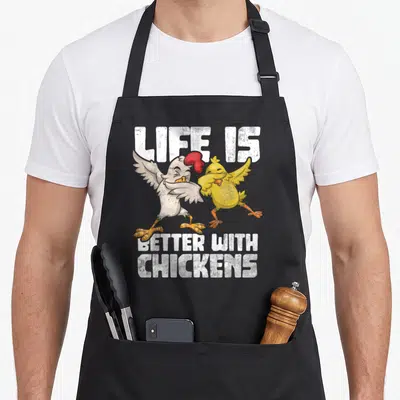 Tablier de cuisine noir avec illustration d'un poulet blanc et d'un poussin jaune dansant sous le texte Life Is Better With Chickens en blanc.