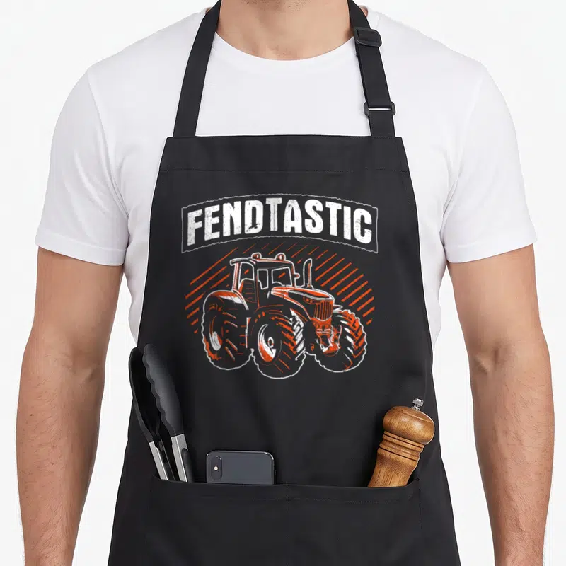 Tablier de cuisine noir avec illustration d'un tracteur orange et du texte Fendtastic en lettres blanches stylisées.