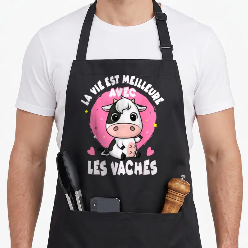 Tablier de cuisine noir avec une vache cartoon rose et blanche et le texte la vie est meilleure avec les vaches