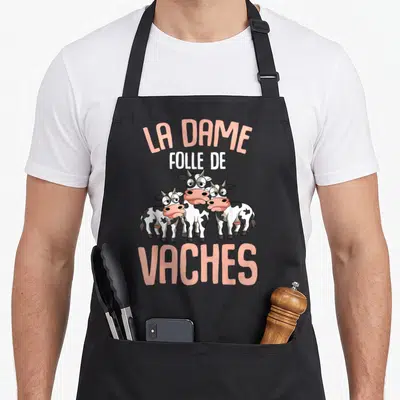 Tablier de cuisine noir avec trois vaches dessinées et le texte La Dame Folle de Vaches en rose et blanc.