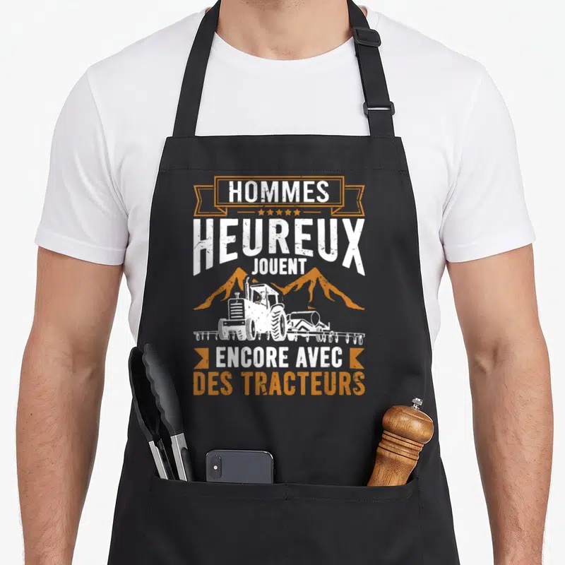 Tablier de cuisine noir avec illustration de tracteur blanc et texte orange sur fond gris uni