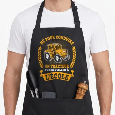Tablier de cuisine noir avec illustration de tracteur orange encadré par des épis de wheat et le texte né pour conduire un tracteur forcé d'aller à l'école.