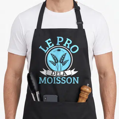 Tablier de cuisine noir avec logo circulaire bleu ciel Le Pro Dela Moisson et épis de wheat stylisés.
