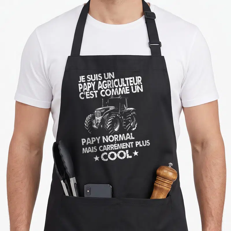 Tablier de cuisine noir avec illustration de tracteur et phrase humoristique sur le statut de papy agricole.