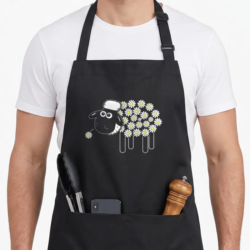 Tablier de cuisine noir avec illustration mouton laine sombre formé de marguerites blanches et jaunes.