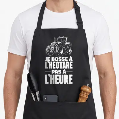 Tablier de cuisine noir avec illustration de tracteur et texte blanc Je bosse à l'hectare pas à l'heure