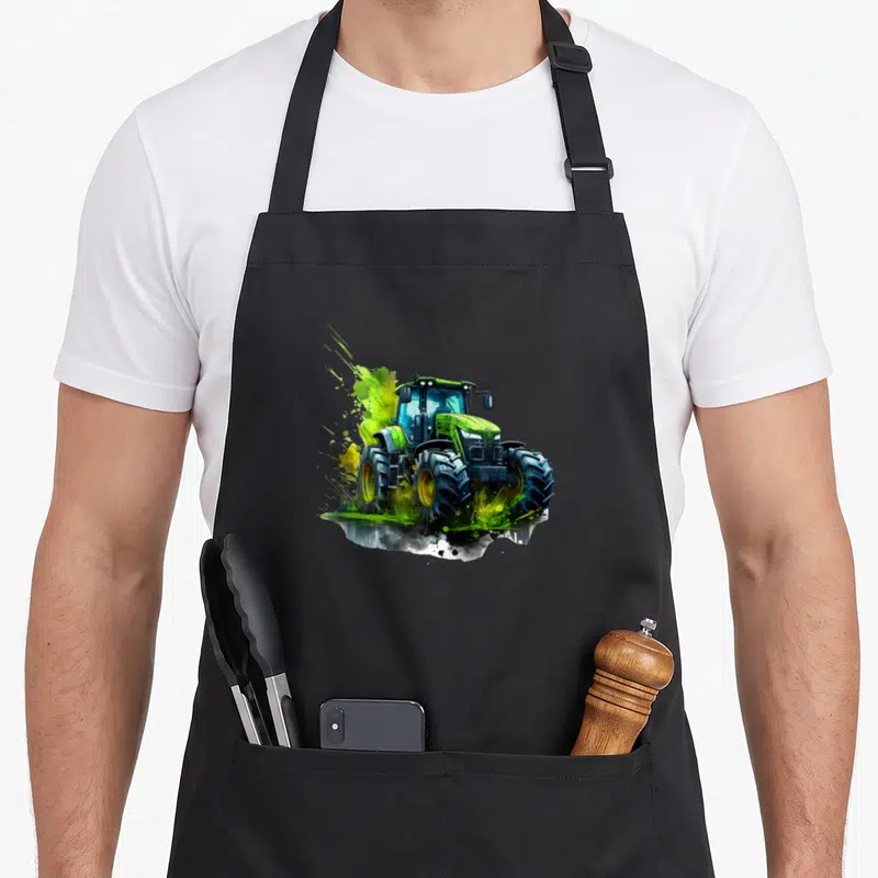 Tablier de cuisine noir avec illustration colorée d'un tracteur agricole vert et jaune aux roues imposantes.