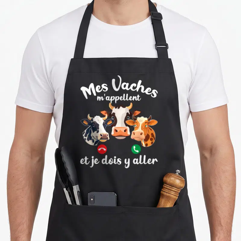 Tablier de cuisine noir avec trois têtes de vaches colorées et texte blanc humoristique sur fond uni.