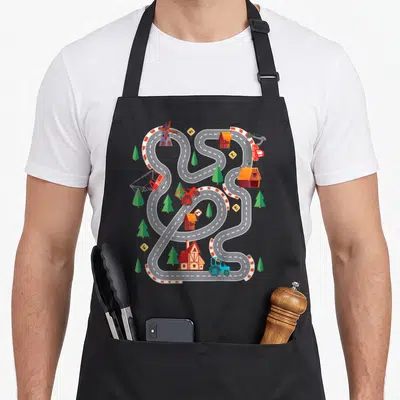 Tablier de cuisine noir avec illustration d'un circuit de ferme jouet comportant des tracteurs et des bâtiments agricoles.