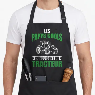 Tablier de cuisine noir avec illustration d'un tracteur et le texte Les Papys Cools Conduisent Un Tracteur en vert et blanc.