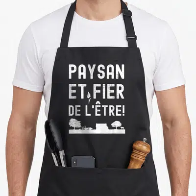Tablier de cuisine noir avec inscription blanche « PAYSAN ET FIER DE L'ÊTRE » et silhouette de ferme en bas.