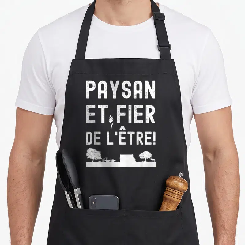 Tablier de cuisine noir avec inscription blanche « PAYSAN ET FIER DE L'ÊTRE » et silhouette de ferme en bas.