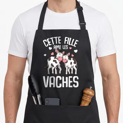 Tablier de cuisine noir avec deux vaches dessinées s'encourageant et le texte Cette Fille Aime Les Vaches Enfant en blanc.