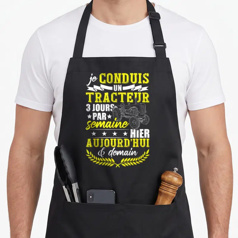 Tablier de cuisine noir avec inscription humoristique sur l'utilisation du tracteur et dessin vintage d'engin agricole.