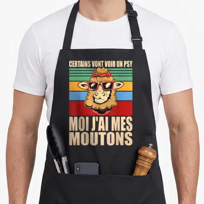 Tablier de cuisine noir avec un mouton portant des lunettes rouges et un bandeau vintage coloré.