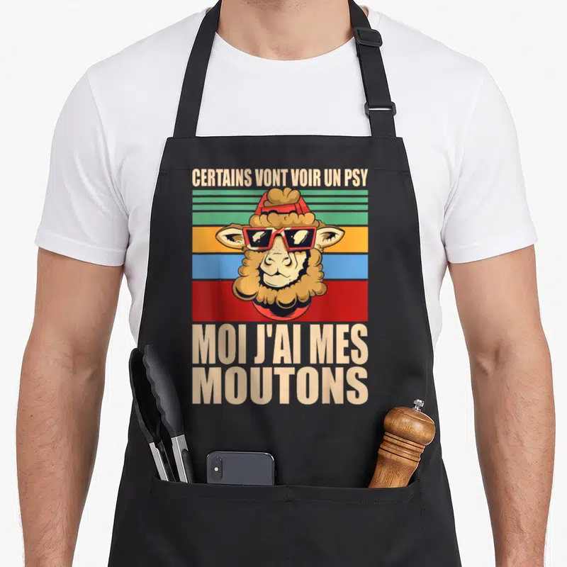 Tablier de cuisine noir avec un mouton portant des lunettes rouges et un bandeau vintage coloré.