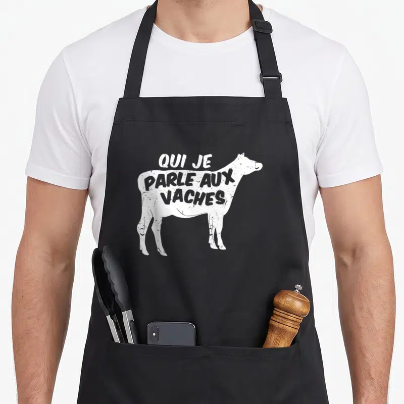 Tablier de cuisine noir avec silhouette de vache blanche et inscription qui je parle aux vaches en lettres capitales blanches.