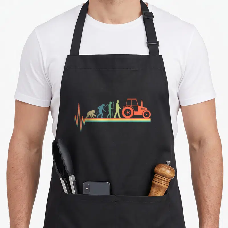 Tablier de cuisine noir avec silhouette évolutive menant à un tracteur orange et une ligne de vie multicolore.