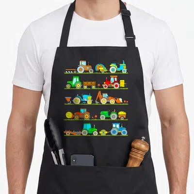 Tablier de cuisine noir avec cinq rangées de tracteurs colorés et d'outils agricoles sur fond de verdure.