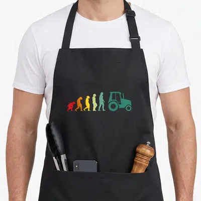 Tablier de cuisine noir avec une illustration colorée montrant l'évolution humaine finissant par un tracteur vert stylisé.