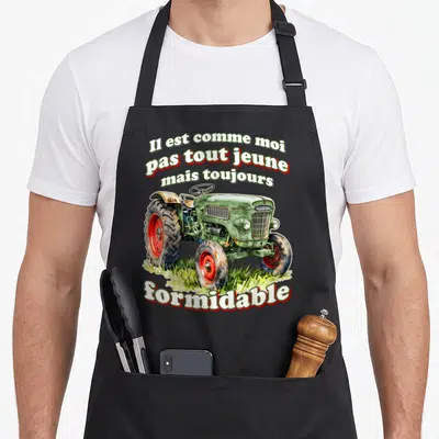 Tablier de cuisine noir avec illustration d'un vieux tracteur vert et texte Il est comme moi pas tout jeune mais toujours formidable.