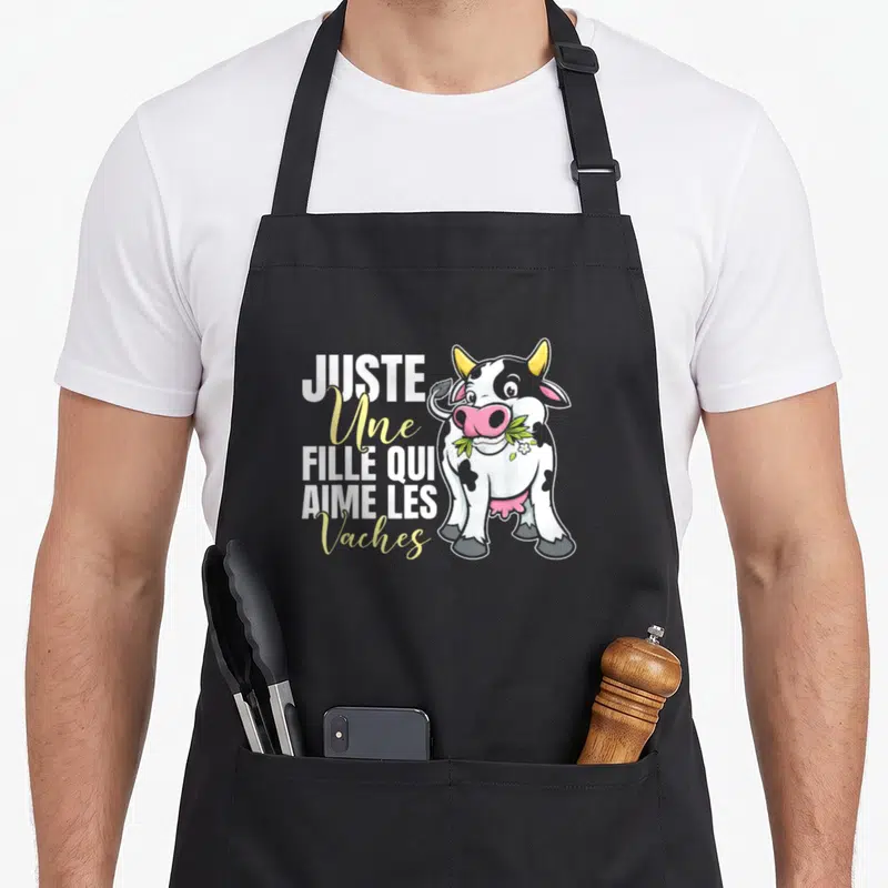 Tablier de cuisine noir avec une vache dessinée et le texte Juste une fille qui aime les vaches en blanc et jaune.