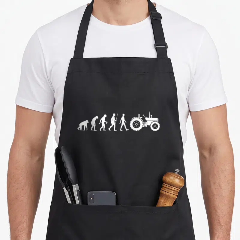 Tablier de cuisine noir avec illustration blanche représentant l'évolution humaine se terminant par un tracteur agricole.
