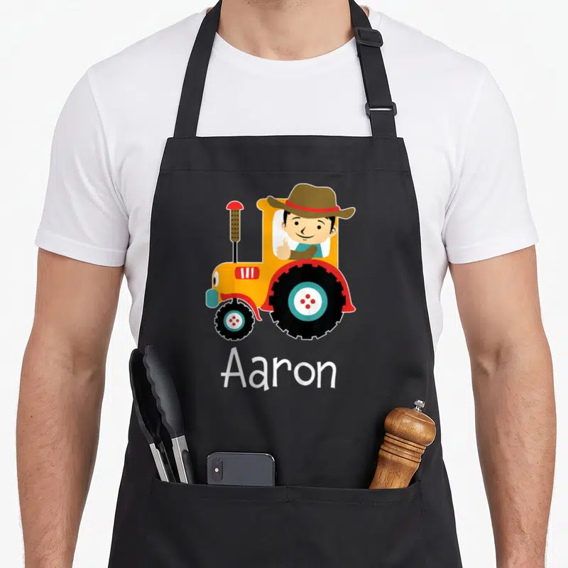 Tablier de cuisine noir avec illustration d'enfant Aaron au volant d'un tracteur jaune et chapeau marron.