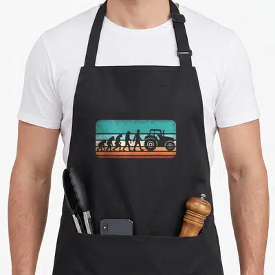 Tablier de cuisine noir avec illustration rétro évolution humaine vers tracteur sur bandes colorées.