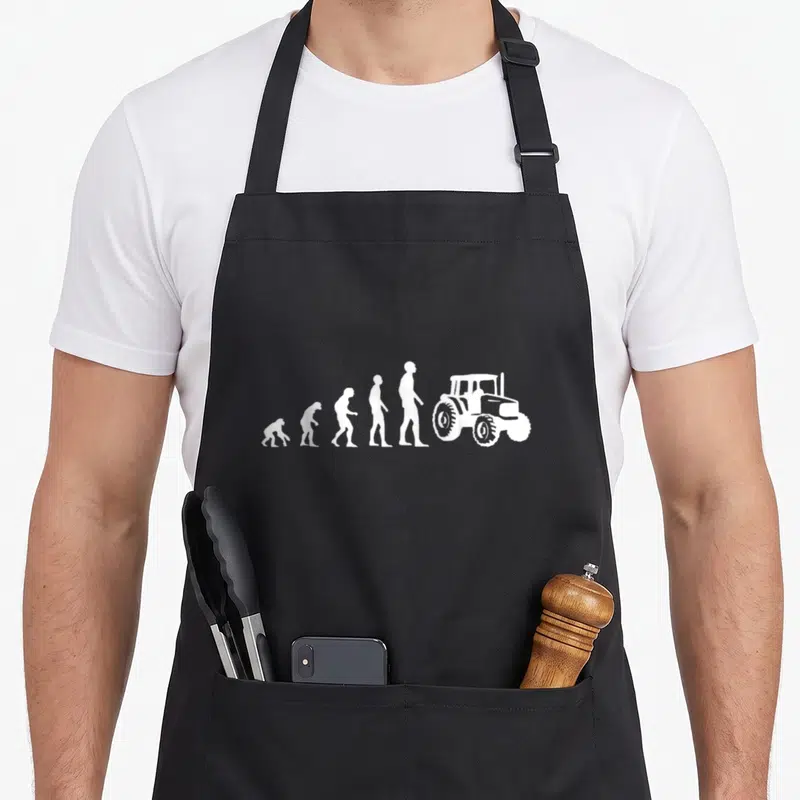 Tablier de cuisine noir avec silhouette blanche évoluant vers un tracteur agricole stylisé.
