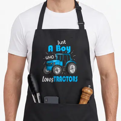 Tablier de cuisine noir avec illustration d'enfant conduisant un tracteur bleu et texte blanc et cyan.