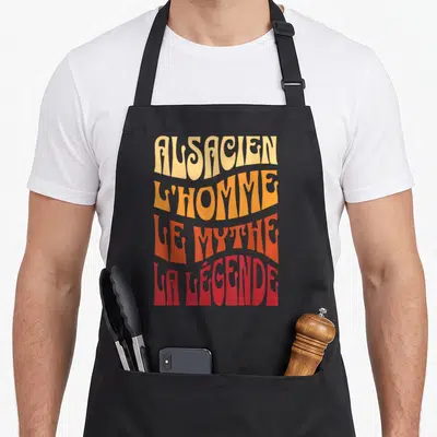 Tablier de cuisine noir avec inscription colorée Alsacien l'homme le mythe la légende en lettres stylisées.