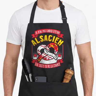 Tablier de cuisine noir avec un bretzel stylisé aux couleurs du drapeau alsacien et un texte humoristique en rouge et jaune.