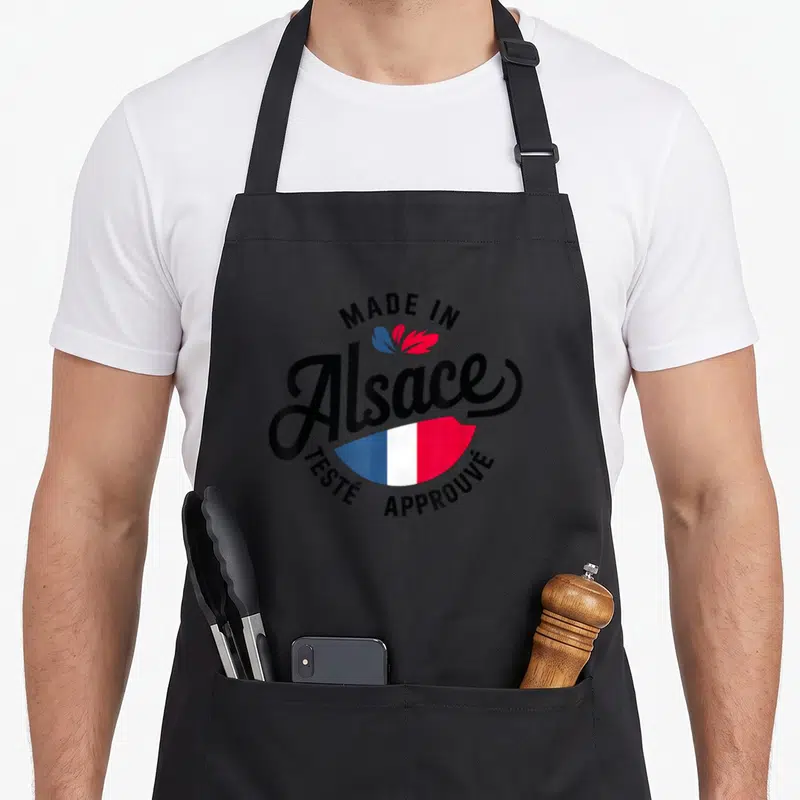 Tablier de cuisine noir avec logo circulaire « Made In Alsace Testé Approuvé » aux couleurs du drapeau français.
