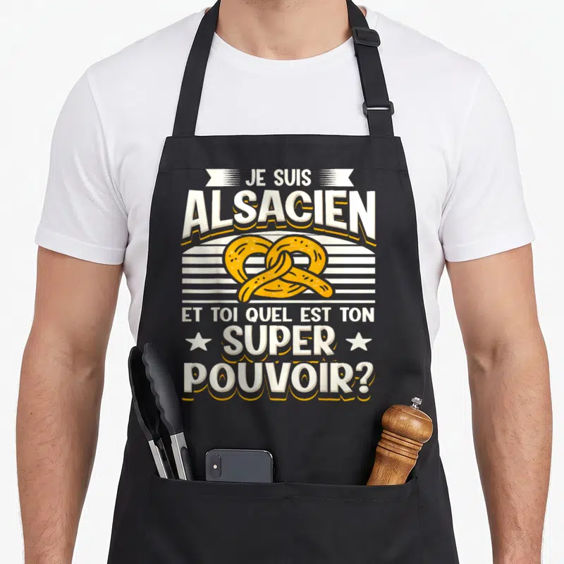 Tablier de cuisine noir avec inscription Je suis Alsacien et illustration d'un bretzel jaune au centre du motif imprimé.
